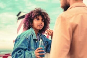 A young girl attentively listens to a young man while holding a glass bottle.