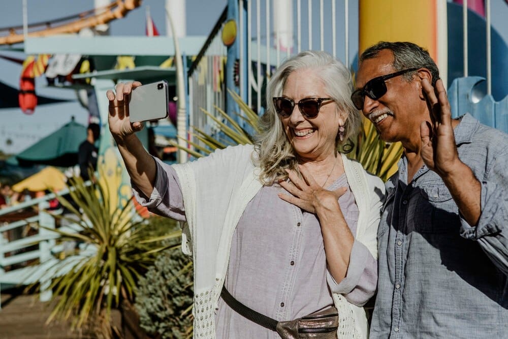 A smiling senior couple takes a selfie together at an amusement park.