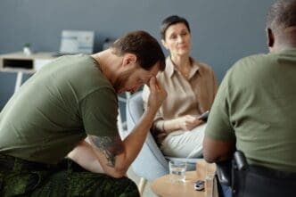 A soldier in uniform sits with their head in their hands, conveying a sense of sadness or despair.