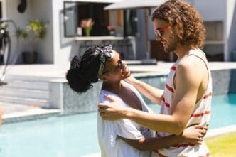 Young African American woman and Caucasian man embrace beside a pool.