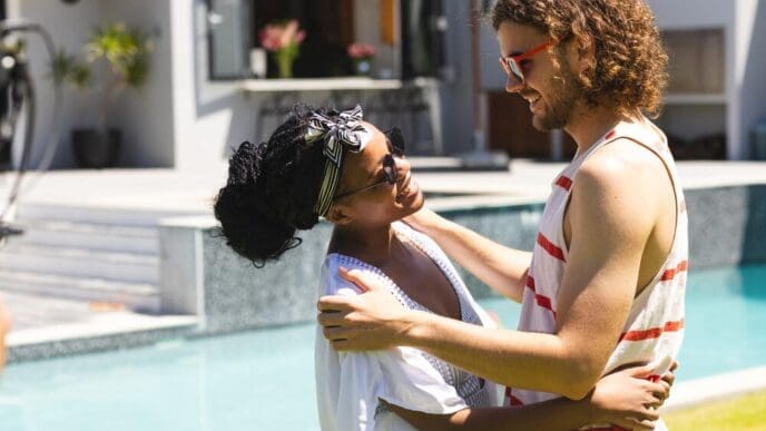 Young African American woman and Caucasian man embrace beside a pool.