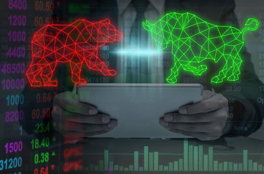 Double exposure of a businessman's hand holding a polygonal bull and bear shape, overlaid with writing.