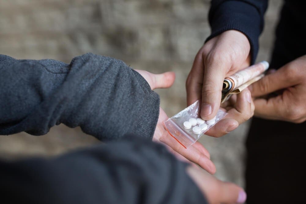 An addict exchanges money with a dealer on a street, representing drug trafficking and addiction.