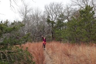 Young woman with a backpack hikes on a trail, smiling and giving a peace sign.