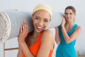 Two women carry a rolled-up rug, likely after moving into a new home.