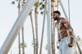 A muscular man does a workout on the beach, likely exercising with the ocean in the background.