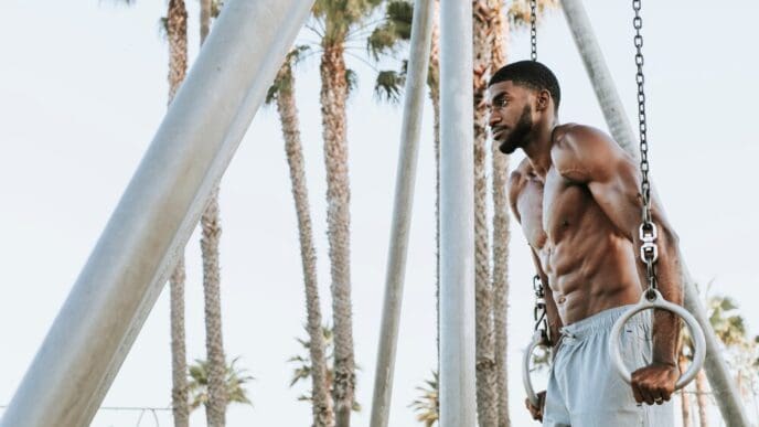 A muscular man does a workout on the beach, likely exercising with the ocean in the background.