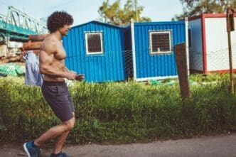 A shirtless young man with a muscular build runs through a city at dusk.