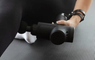 A woman massages her glutes with a percussive massage gun.