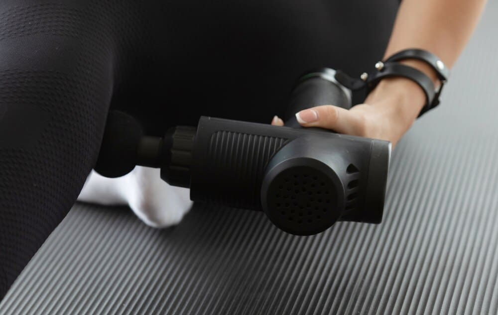 A woman massages her glutes with a percussive massage gun.