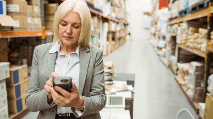 Warehouse manager in a warehouse, using a handheld device while looking intently at the screen.