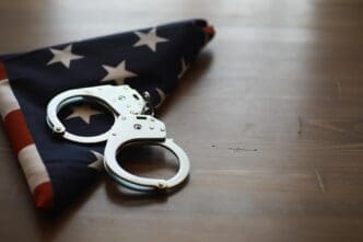 An American flag is folded and placed next to a pair of handcuffs on a wooden table, representing the intersection of law and patriotism.