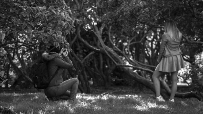 A friend takes a photo of a woman with a camera in a field.