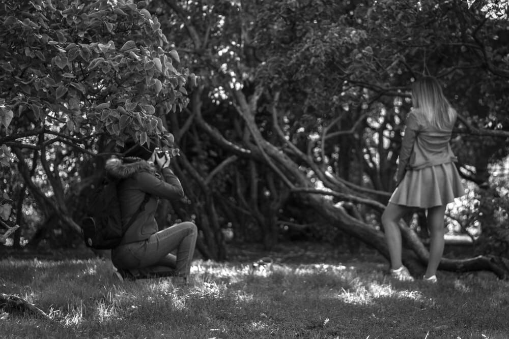 A friend takes a photo of a woman with a camera in a field.