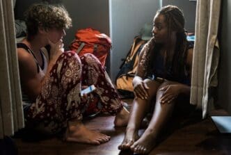 Two friends sit on a wooden floor, engaged in conversation.