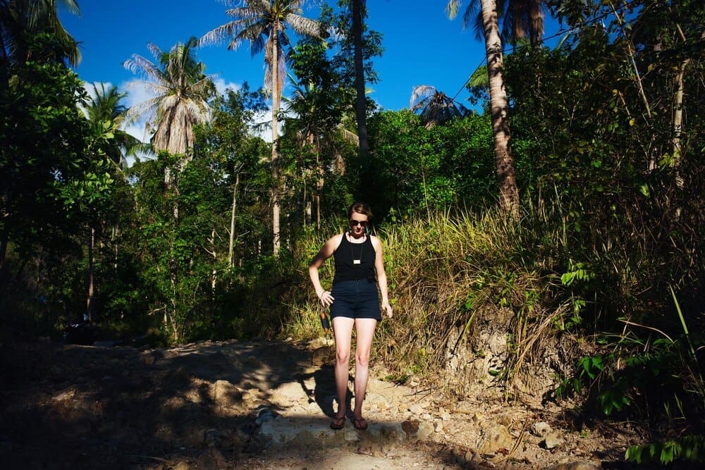 Young woman stands with her back to trees.