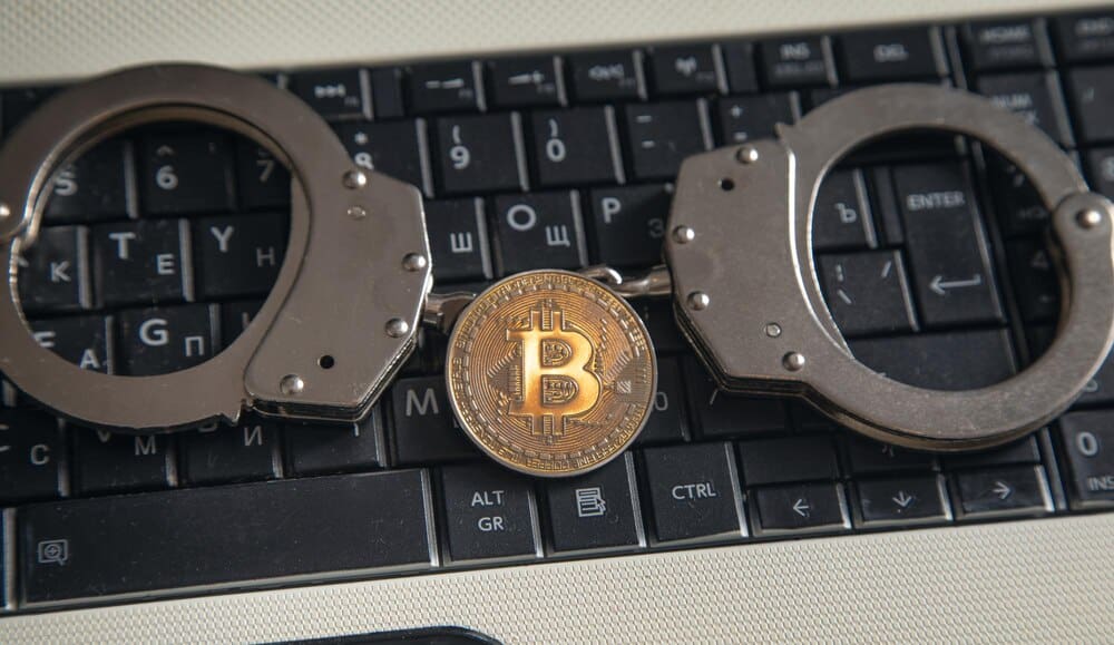 A gold bitcoin sits next to a pair of handcuffs, representing virtual currency.