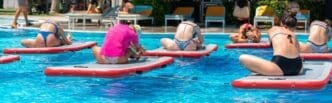 People practice yoga on paddleboards in a resort pool, illustrating tropical fitness and relaxation.
