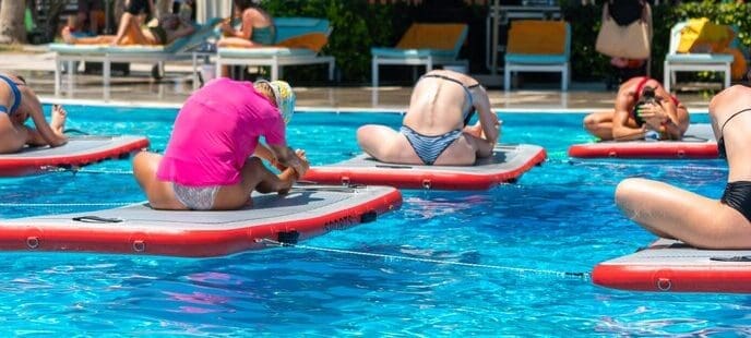 People practice yoga on paddleboards in a resort pool, illustrating tropical fitness and relaxation.