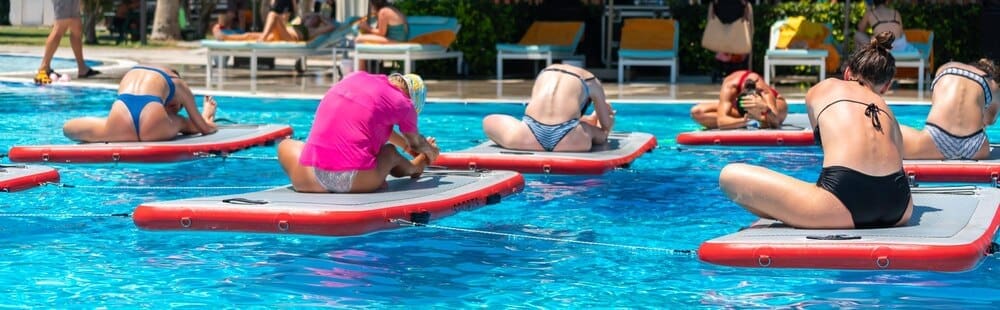 People practice yoga on paddleboards in a resort pool, illustrating tropical fitness and relaxation.