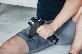 A young, sporty man practices self-massage on his hands with a percussion massager.
