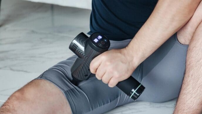 A young, sporty man practices self-massage on his hands with a percussion massager.