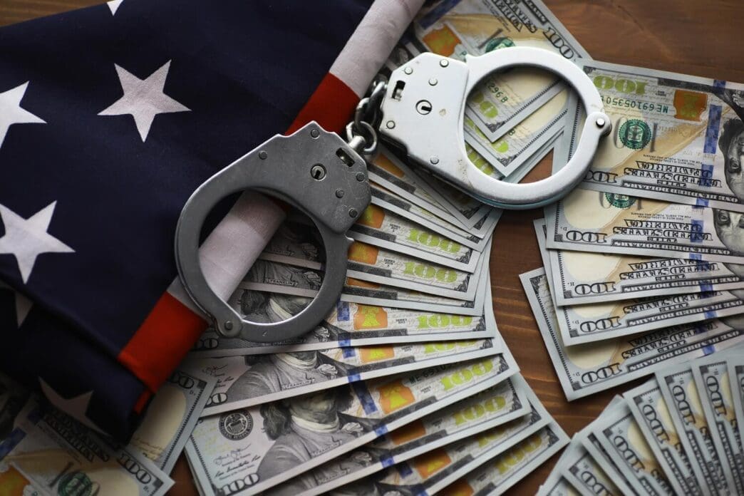 Handcuffs rest on an American flag and a stack of dollar bills, representing crime and punishment in the United States.