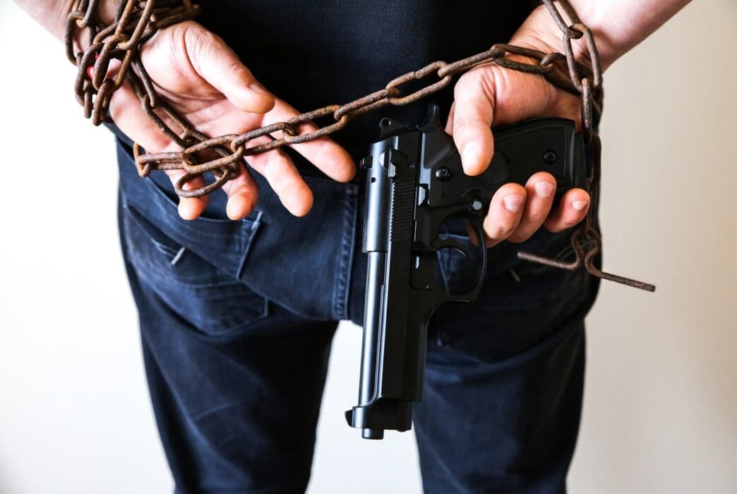 Hands restrained in rusty chains holding a handgun, depicting a criminal arrest.