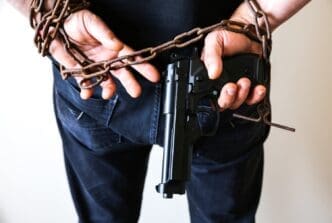 Hands restrained in rusty chains holding a handgun, depicting a criminal arrest.