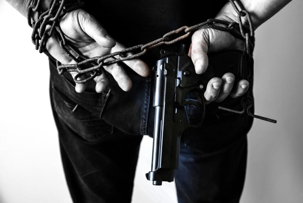 Hands bound in rusty chains, holding a gun, depicting a criminal arrest.