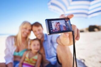 A smiling family of three takes a selfie on a beach.