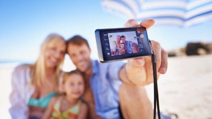 A smiling family of three takes a selfie on a beach.