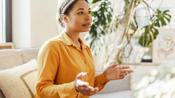 Happy African American woman smiling while using sign language by a window in a cozy home.