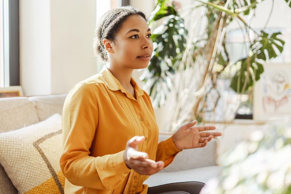 Happy African American woman smiling while using sign language by a window in a cozy home.