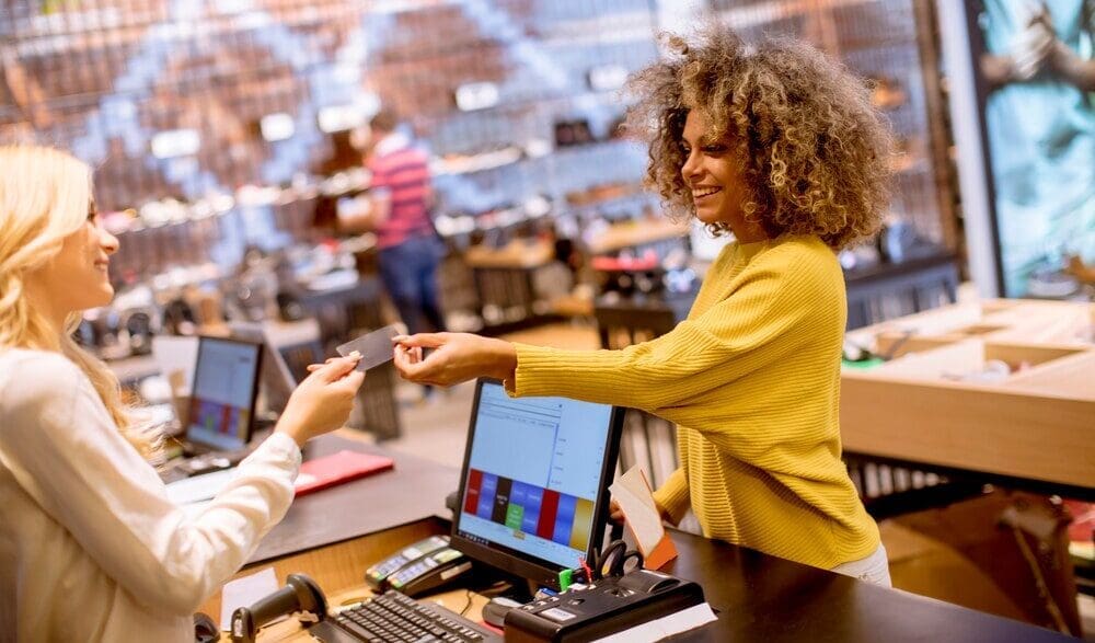 A smiling woman uses a credit card to pay for a purchase at a fashion showroom.