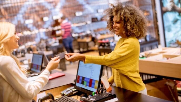 A smiling woman uses a credit card to pay for a purchase at a fashion showroom.