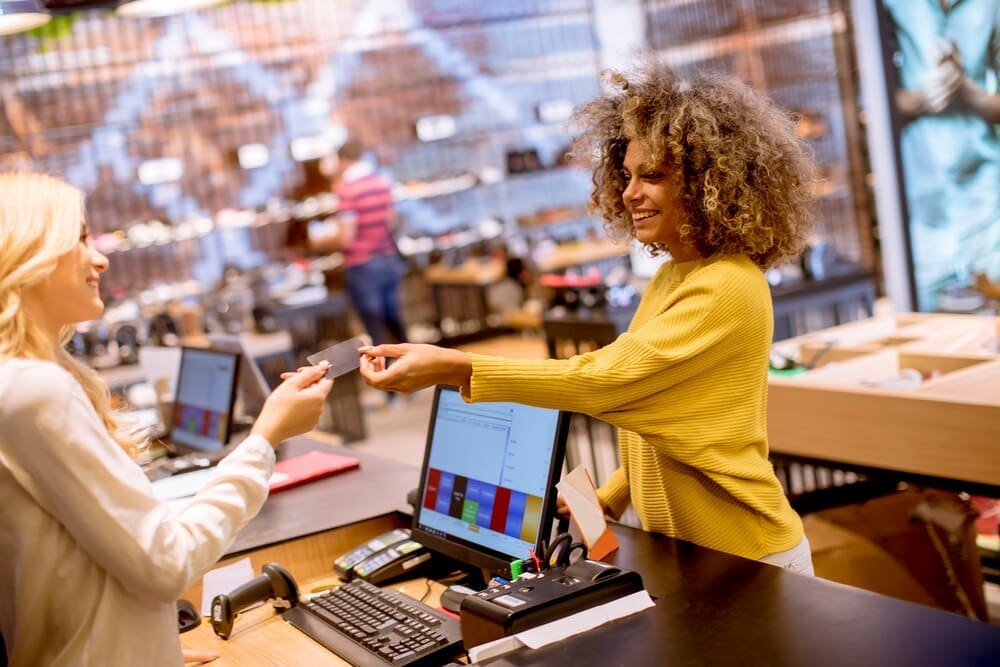 A smiling woman uses a credit card to pay for a purchase at a fashion showroom.