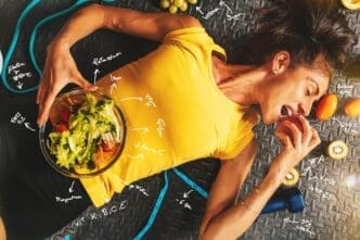 A smiling woman eats a healthy snack while training in a gym.