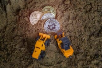 High-angle shot of a collection of Bitcoin cryptocurrency coins and toy trucks arranged on dirt.