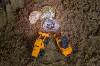 High-angle shot of a collection of Bitcoin cryptocurrency coins and toy trucks arranged on dirt.