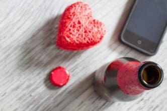 High-angle shot of an open beer bottle, a smartphone, and a wooden heart arranged on a plank.