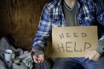 A man experiencing homelessness holds a sign, seeking assistance.