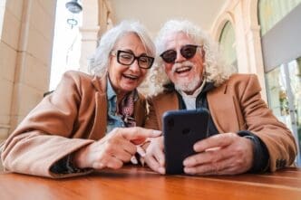 A smiling senior couple shares a smartphone, appearing joyful as they browse apps together.