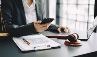 A male judge in a courtroom uses a smartphone while holding a gavel.