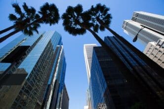 Downtown Los Angeles skyscrapers are framed by palm trees.
