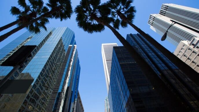 Downtown Los Angeles skyscrapers are framed by palm trees.
