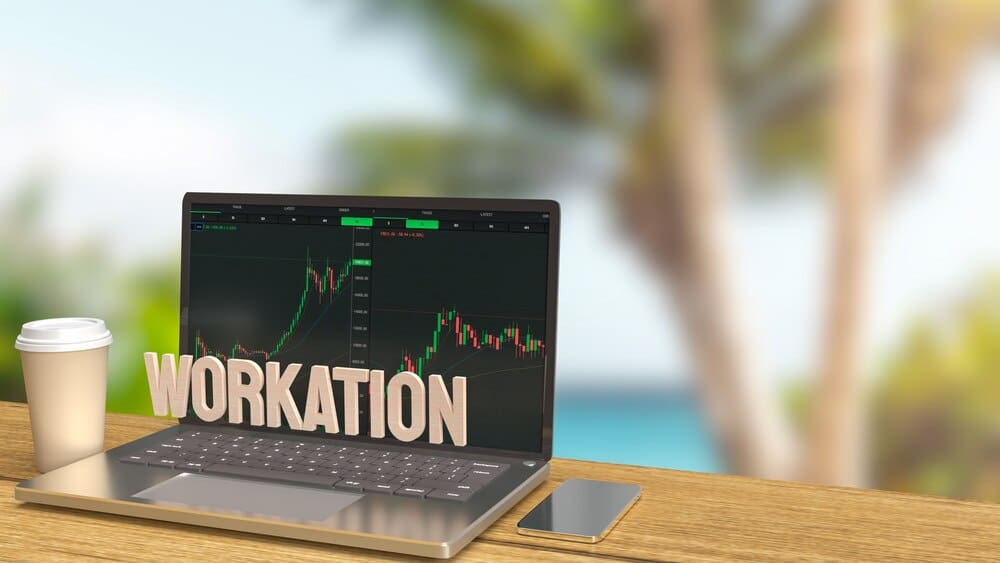 A 3D rendering depicts a laptop open on a wooden table outdoors, suggesting a workation concept.