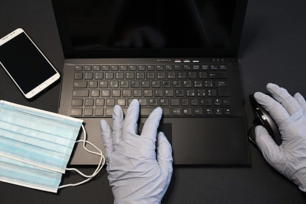 A person's hands typing on a laptop keyboard, seen from the waist down, resting on a table.
