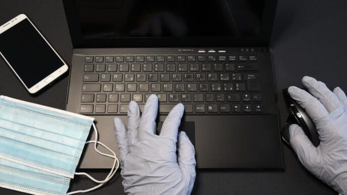 A person's hands typing on a laptop keyboard, seen from the waist down, resting on a table.
