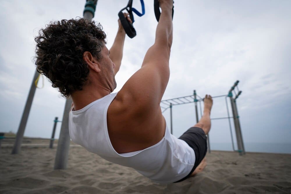 A man does push-ups on the sandy beach with the ocean in the background.
